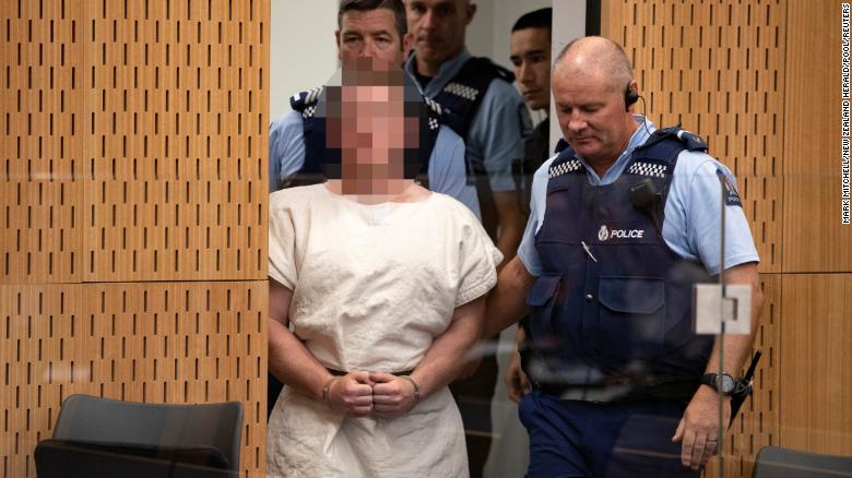 Tarrant is escorted into Christchurch District Court on Saturday. The judge ruled pictures of the suspect in court must have his face blurred.