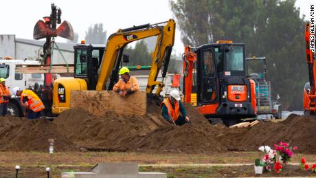 Diggers work behind a white screen fence to dig graves for some of the 50 people who died in Friday's terror attack.