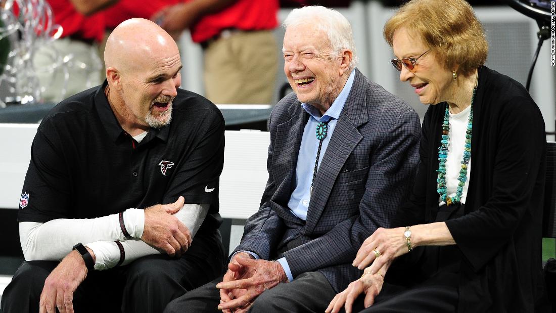 Carter and his wife, Rosalynn, speak with Atlanta Falcons head coach Dan Quinn prior to an NFL game in September 2018.