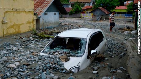 A car sits abandoned in the mud on a flooded street.