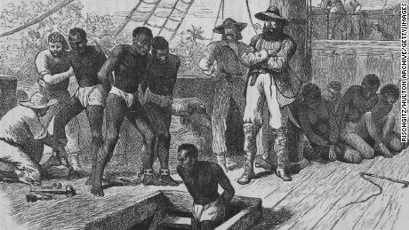 An illustration shows slaves being shackled on board a slave ship.