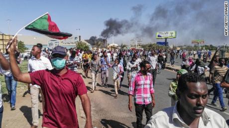 Sudanese protesters waive the national flag as they march toward the army headquarters.