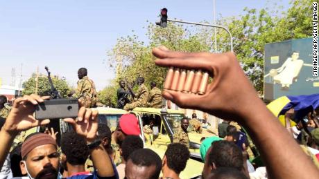 A protester holds bullet cartridges as others gather in front of security forces Monday outside the military headquarters.