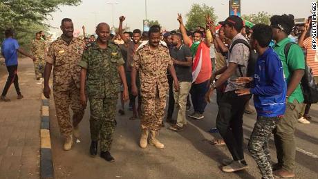Sudanese protesters cheer Thursday for passing soldiers near military headquarters in Khartoum.