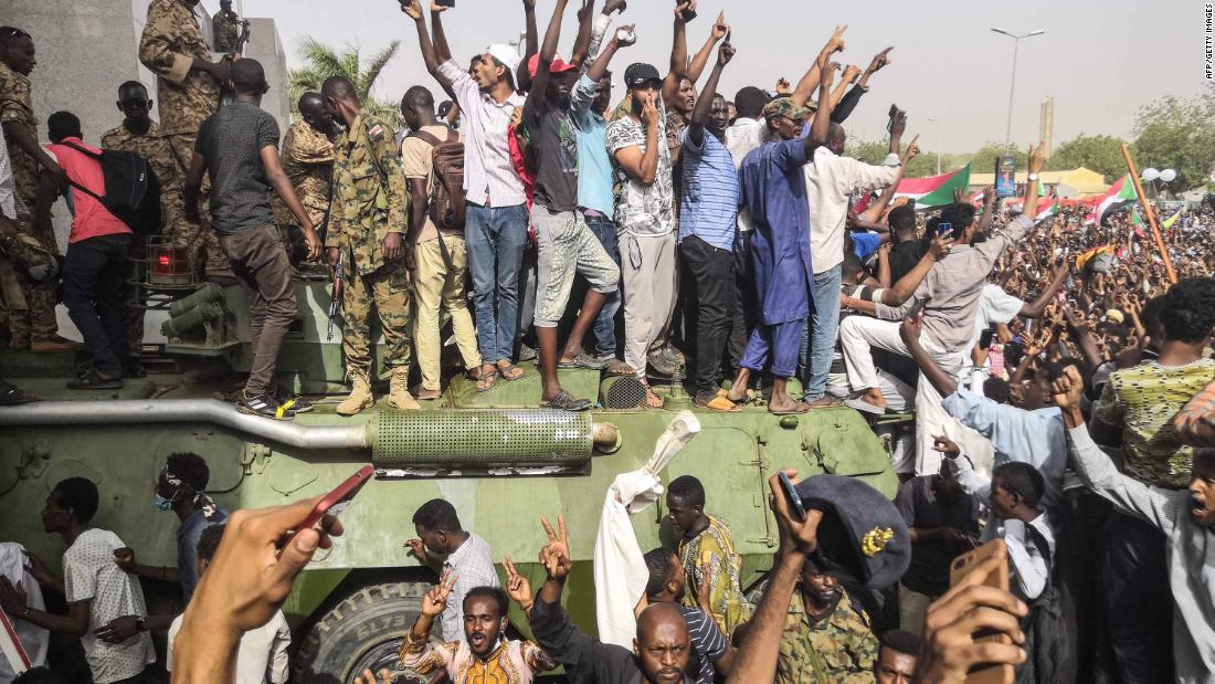 Demonstrators stand on a military vehicle April 11 as they cheer and flash the sign of victory.