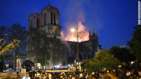 Crowds look on as flames and smoke billow from the roof at Notre-Dame Cathedral in Paris on April 15, 2019. - A fire broke out at the landmark Notre-Dame Cathedral in central Paris, potentially involving renovation works being carried out at the site, the fire service said.Images posted on social media showed flames and huge clouds of smoke billowing above the roof of the gothic cathedral, the most visited historic monument in Europe. (Photo by ERIC FEFERBERG / AFP)