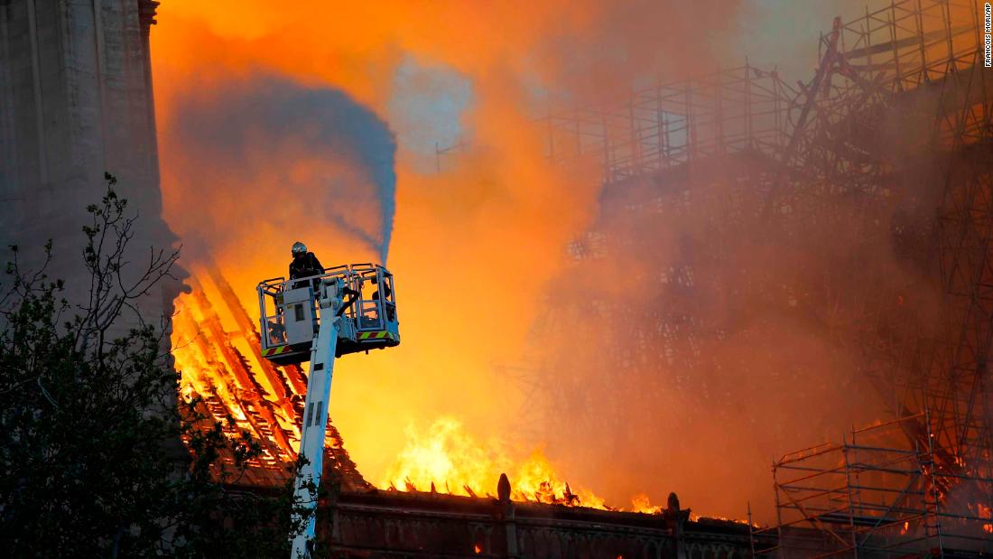 A firefighter uses a hose to tackle the flames as the cathedral&#39;s roof burns.