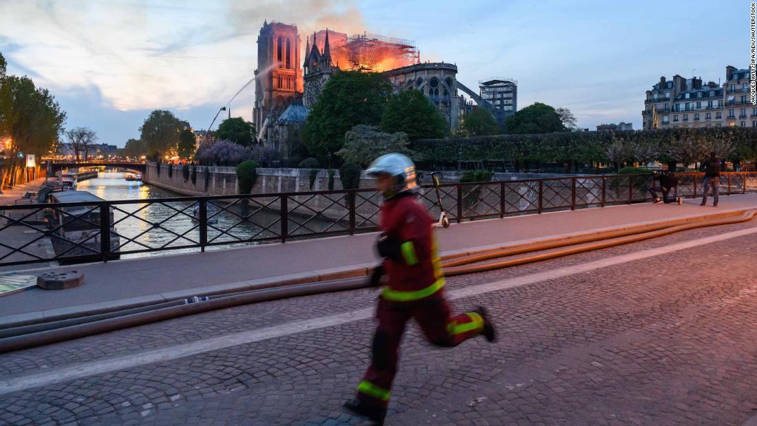 Flames and smoke rise from Notre Dame as a firefighter rushes past.