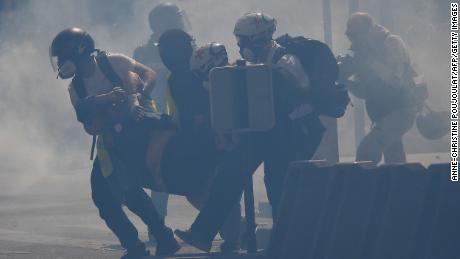 So-called &quot;street medics&quot; carry an injured protester amid tear gas.