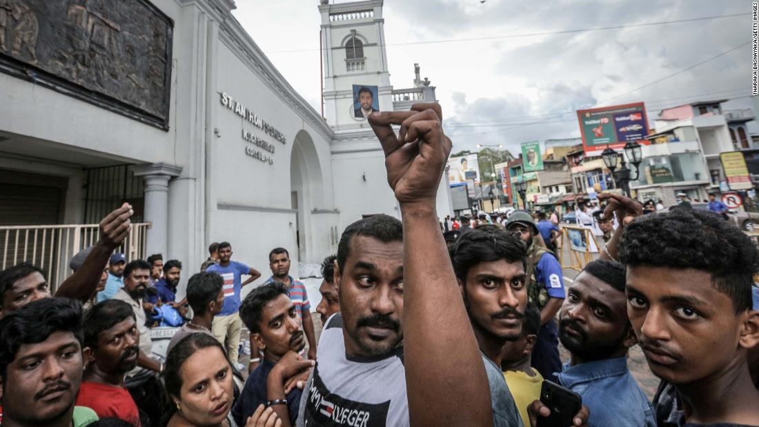 A man holds up a blood-stained photograph as people wait to identify the bodies of their loved ones in front of St. Anthony&#39;s Church.