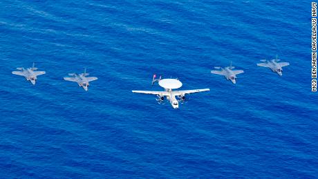 A US Navy carrier-based E-2D Hawkeye airborne radar plane and four US Marine Corps F-35B Lightning jets fly over the South China Sea.