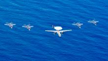 A US Navy carrier-based E-2D Hawkeye airborne radar plane and four US Marine Corps F-35B Lightning jets fly over the South China Sea.