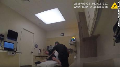 A Broward sheriff&#39;s deputy tries to restrain a suspect who is handcuffed to a hospital bed.