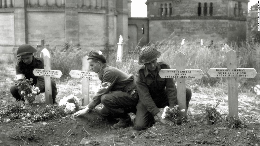 Canadian soldiers place flowers on temporary graves for allied soldiers in Normandy.