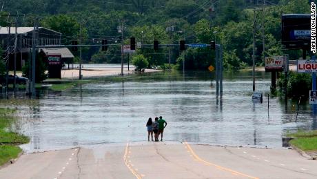 People stand in the middle of the street and look out over the flooded Massard Creek in Arkansas.