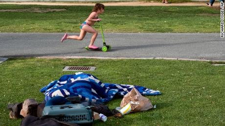 In this Monday, June 3, 2019 photo a child rides her scooter past a homeless person covered under a blanket in Santa Monica, Calif. The number of homeless people counted across Los Angeles County jumped 12% over the past year to a total of 58,936. The Los Angeles Homeless Services Authority presented the results of January's annual count to the Board of Supervisors on Tuesday, June 4.  (AP Photo/Richard Vogel)