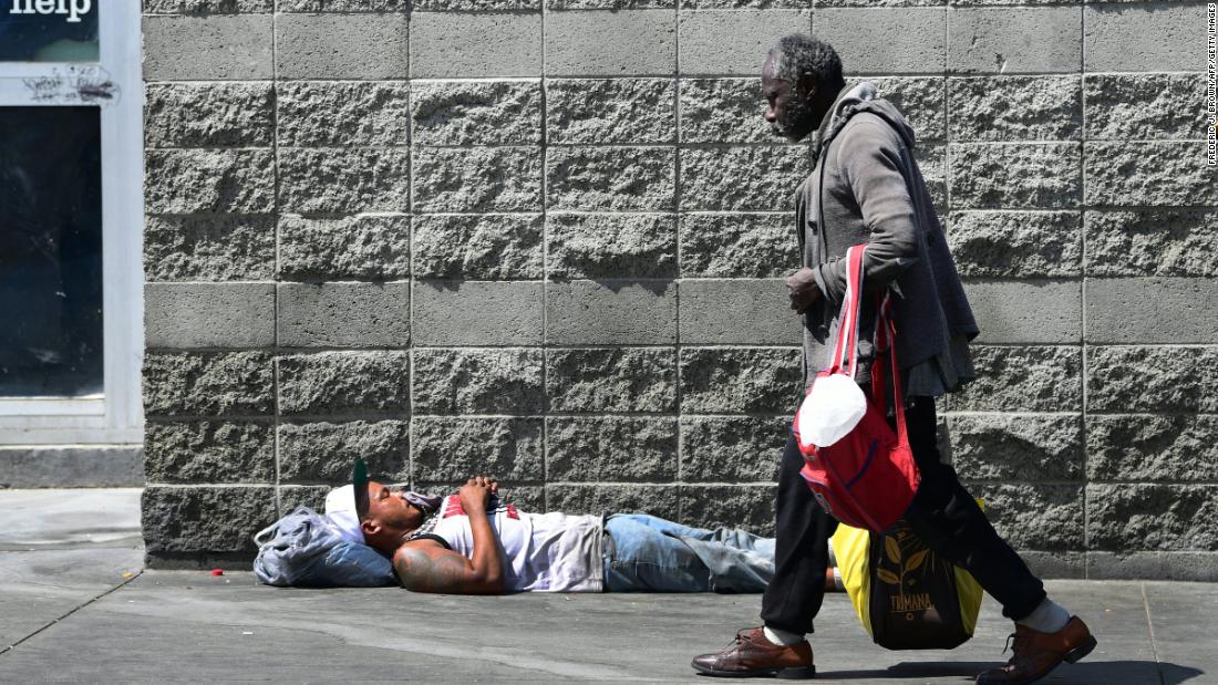 A pedestrian walks past a man sleeping on a sidewalk in Los Angeles on May 30.