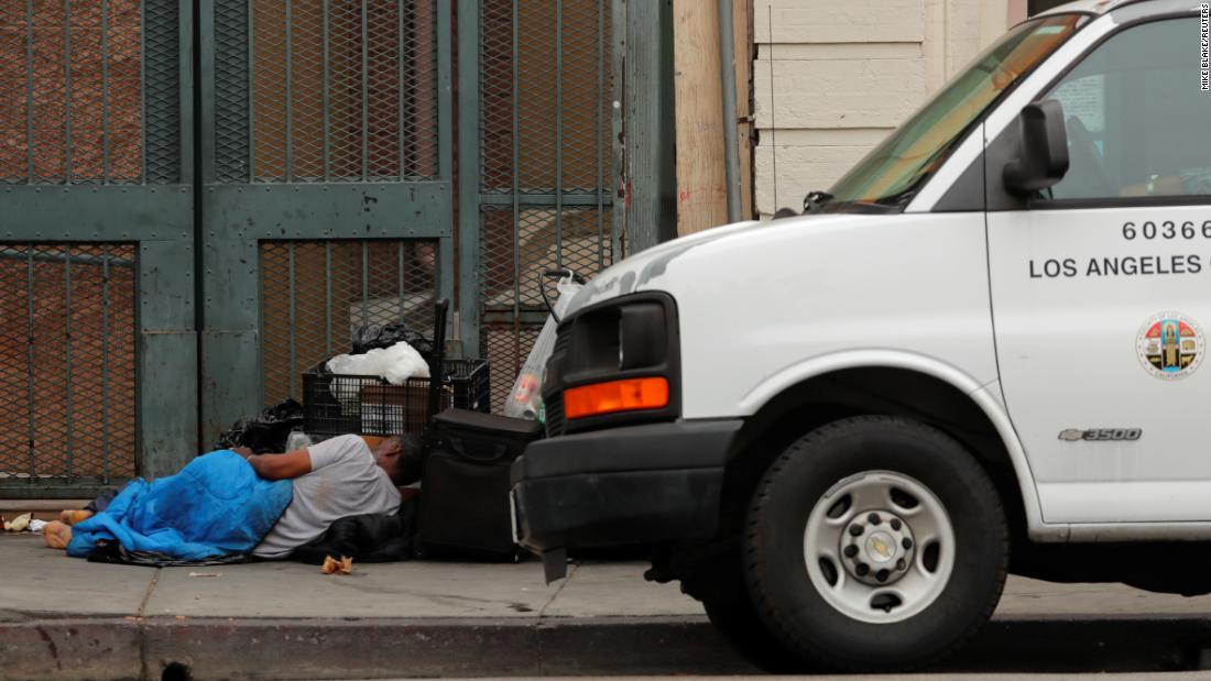 A homeless person sleeps on the sidewalk next to a Los Angeles County vehicle on June 4.