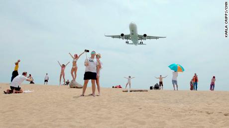 Tourists pose for photographs as an airplane descends into Phuket International Airport.  