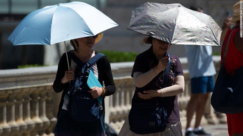 Tourists walk under umbrellas to protect themselves from the sun on a warm summer day in Barcelona on June 28.