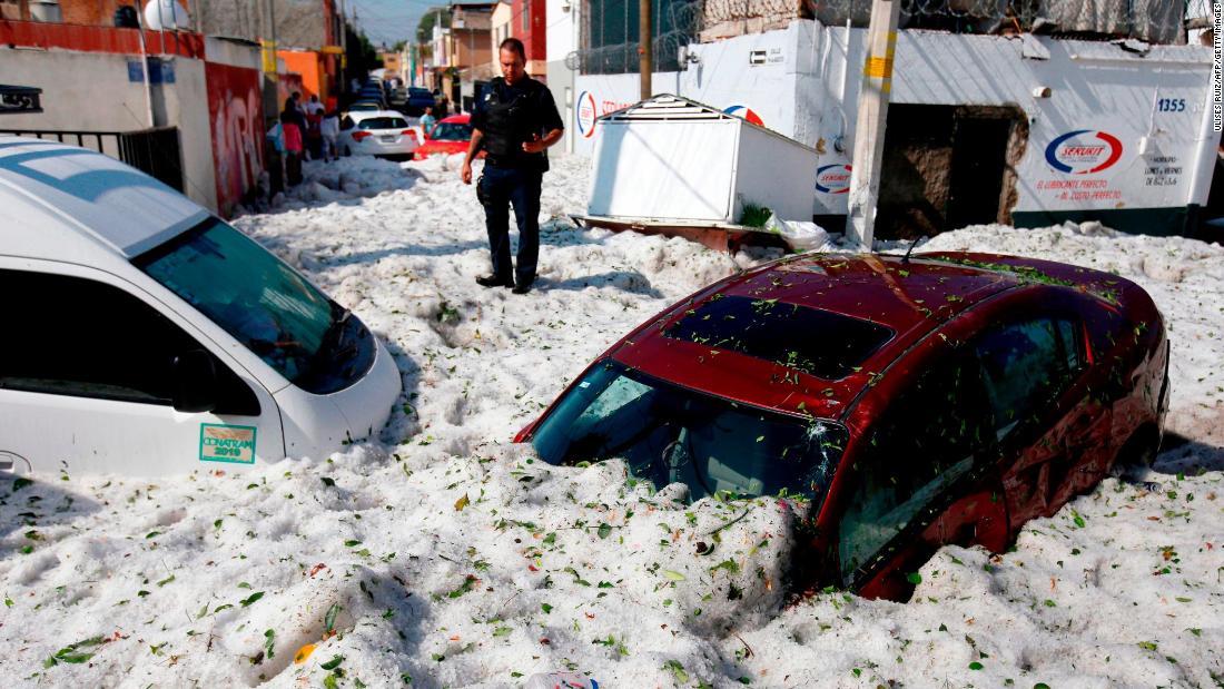 A police officer stands next to vehicles buried in ice.