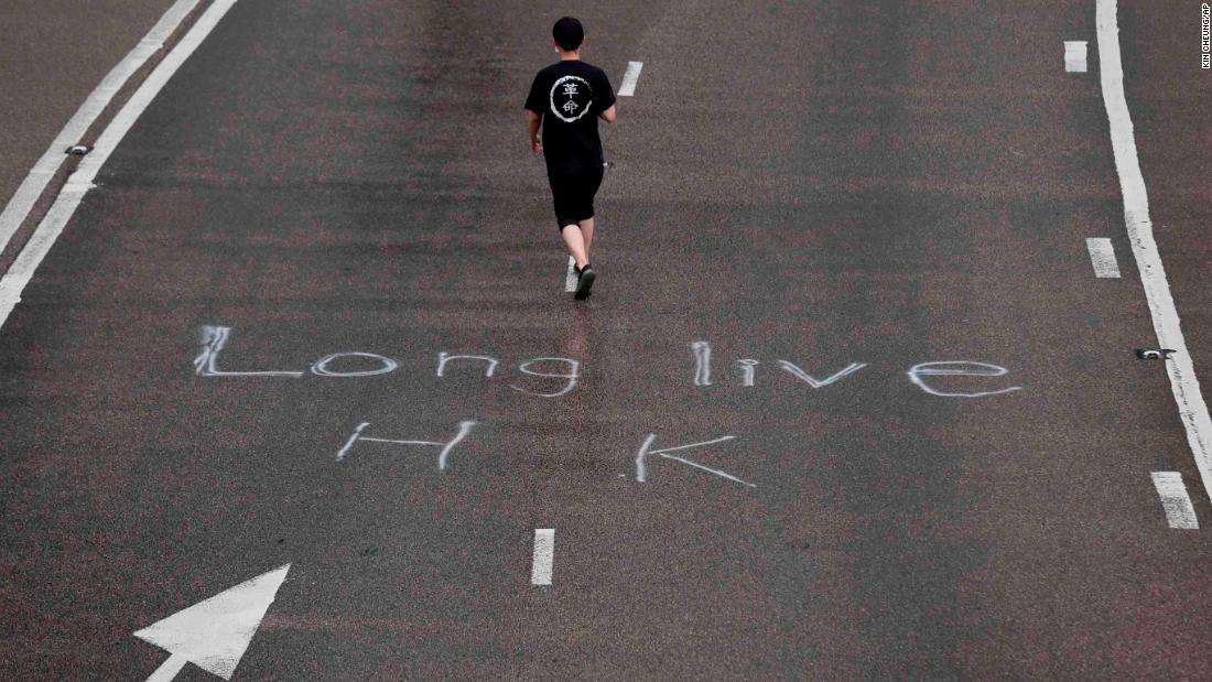 A protester wearing a T-shirt with the word "revolution" walks past an inscription on a road that reads "Long Live HK."