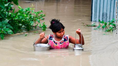 An Indian girl carries drinking water as she wades through flood waters in India&#39;s Assam state on July 15, 2019.