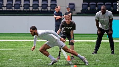 A teen performs in the NFL Academy&#39;s trials, watched by British NFL player Efe Obada (right). 