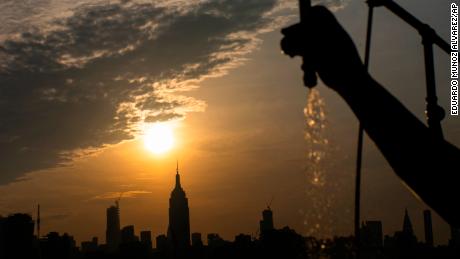 The sun rises over New York City and the Empire State Building while a man sprays water at Pier A.