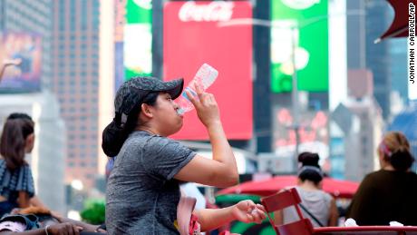 A woman drinks water in Times Square as temperatures reach the mid-to-upper 90s.