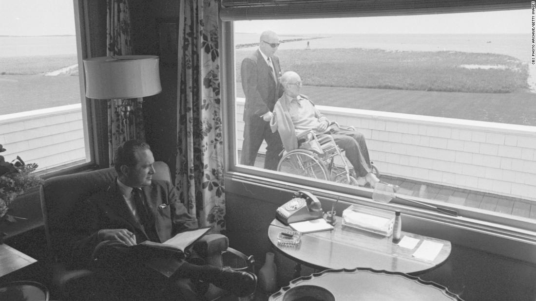 A man in Hyannis Port glances outside a window to see Joseph Sr. being pushed in a wheelchair in 1964. Joseph Sr., a former US ambassador to the United Kingdom, died in 1969.