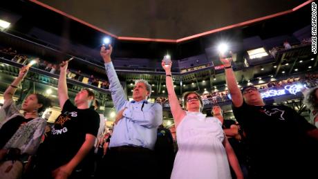 People hold up their cellphones as the names of the victims are read.