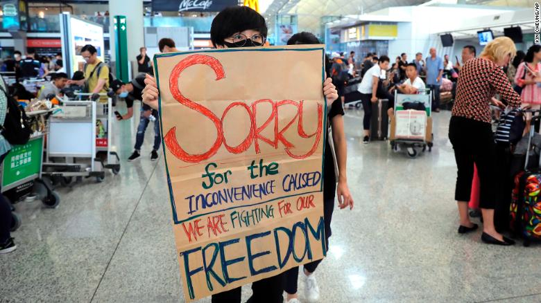 A protester shows a placard to stranded travelers during a demonstration at the Airport in Hong Kong, Tuesday, Aug. 13, 2019.