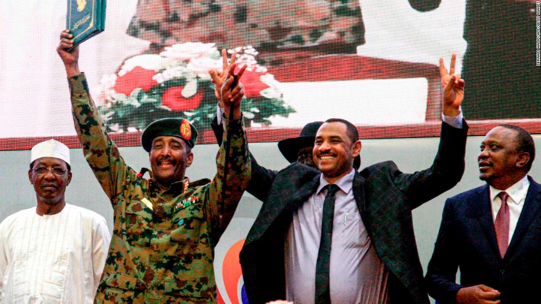 Sudanese protest leader Ahmad Rabie, center right, flashes the victory gesture alongside Gen. Abdel Fattah al-Burhan, the chief of Sudan&#39;s ruling Transitional Military Council, center left, during a ceremony where they signed a constitutional declaration.