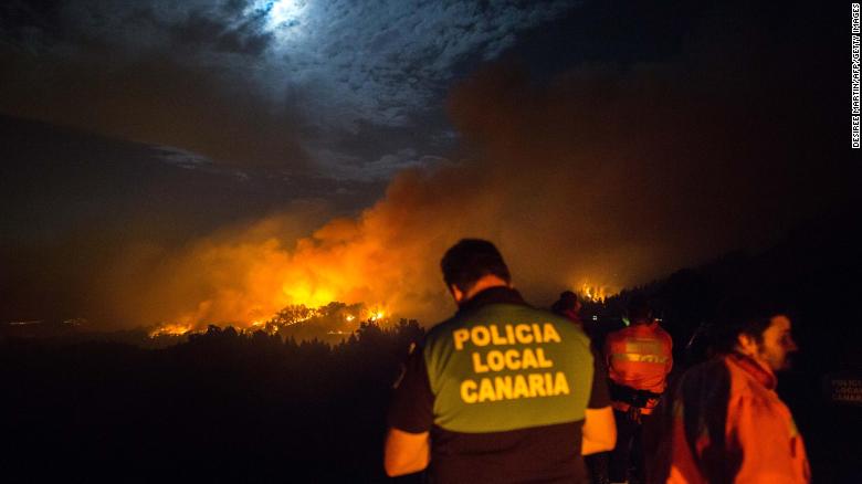 Firemen and policeman watch from the road as a blaze rages in Spain&#39;s Canary Islands on August 17, 2019. 