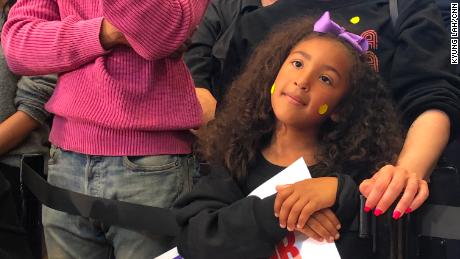 A young girl stands amid a diverse crowd at a Kamala Harris rally in Los Angeles.