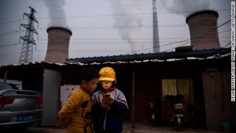  Chinese boys look at their smartphone in front of their house next to a coal fired power plant on the outskirts of Beijing, China.