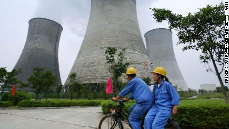 Workers cycle past power stations in Guangan, in southwest China&#39;s Sichuan province.