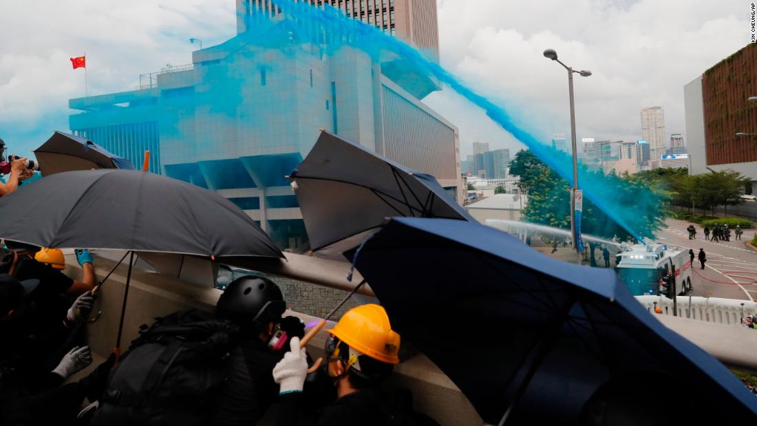 Protesters take cover as policemen fire blue-colored water on them. Blue dye can be used to stain and identify masked protesters.