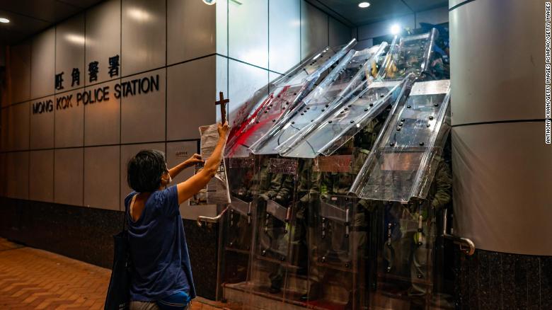 A woman holds a cross in front of the Mongkok Police Station as riot police holding shields stand guard during a standoff with protesters after an anti-government rally in on September 1, 2019, in Hong Kong.