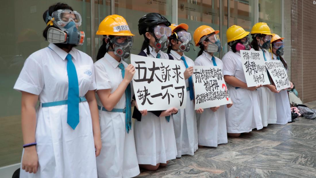 Students wearing gas masks and helmets hold a banner that reads "five major demands are indispensable" at St. Francis' Canossian College in Hong Kong.