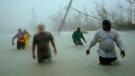 Volunteers walk under the wind and rain from Hurricane Dorian through a flooded road as they work to rescue families near the Causarina bridge in Freeport, Grand Bahama, Bahamas, Tuesday, Sept. 3, 2019. The storm's punishing winds and muddy brown floodwaters devastated thousands of homes, crippled hospitals and trapped people in attics. (AP Photo/Ramon Espinosa)