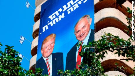 A giant Israeli Likud Party election banner hangs from a building in Tel Aviv showing Netanyahu shaking hands with Trump, with a caption above reading in Hebrew "Netanyahu, in a league of his own."