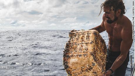 Crew member Josh Muñoz retrieves a plastic basket -- home to some gooseneck barnacles -- from the Great Pacific Garbage Patch.