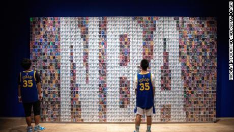 Two Chinese youths stand in front of a wall displaying basketball trading cards at the NBA exhibition in Beijing on August 19, 2019.