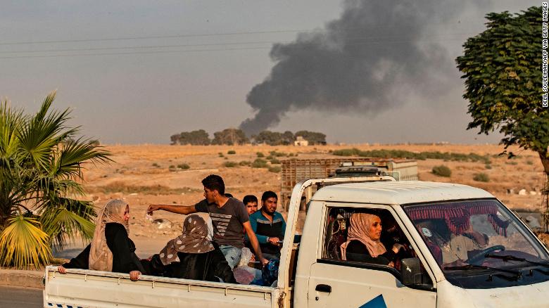 Civilians ride a pickup truck as smoke billows following Turkish bombardment on Syria&#39;s northeastern town of Ras al-Ain.
