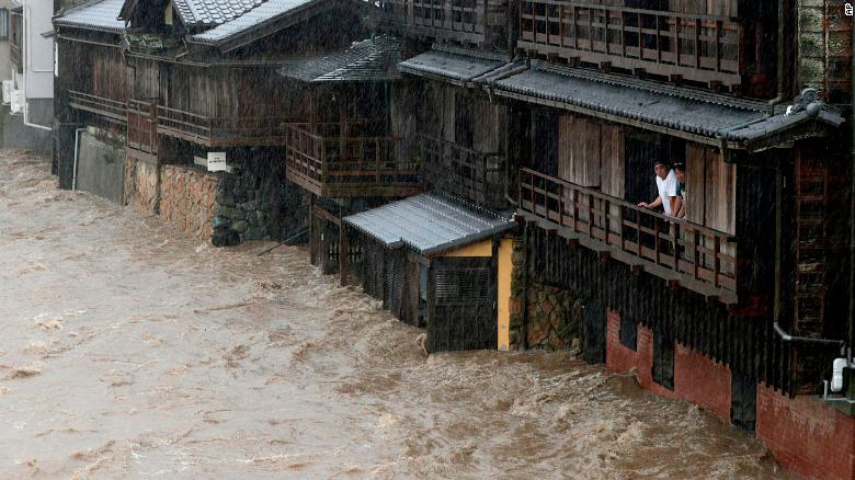 People watch floodwater from the Isuzu river flow by in Ise, Japan, on Saturday, October 12, 2019. (Credit: CNN)