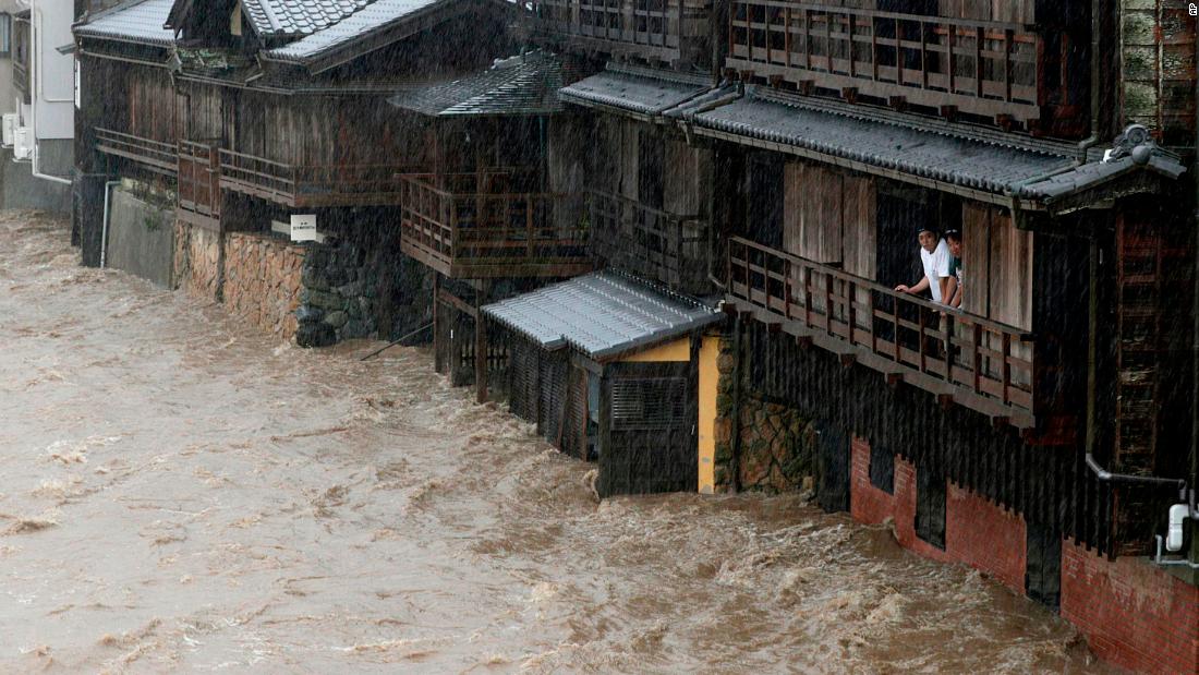 People watch floodwater from the Isuzu river flow by in Ise, Japan, on Saturday, October 12, 2019.