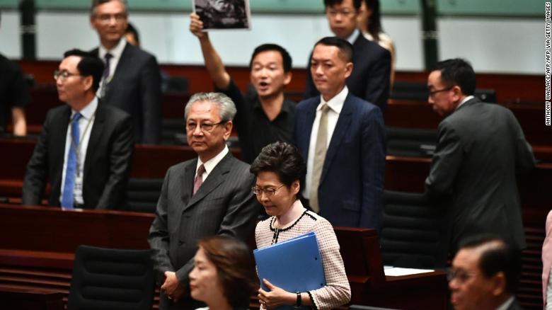 A pro-democracy lawmaker (behind) holds up a placard in protest as Hong Kong&#39;s Chief Executive Carrie Lam (C) walks into the chamber to give her annual policy address at the Legislative Council (Legco) in Hong Kong on October 16, 2019. 