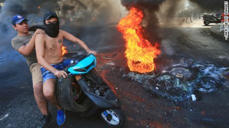Lebanese demonstrators drive past a tire fire during a protest against dire economic conditions in the Lebanese capital Beirut&#39;s southern suburbs on October 17, 2019. - Public anger has simmered since parliament passed an austerity budget in July to help trim a ballooning deficit and flared on Thursday over new plans to tax calls on messaging applications such as Whatsapp, forcing the government to axe the unpopular proposal.